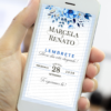 Convite lembrete de casamento azul exibido na tela de um celular, com flores em tons de azul no topo, moldura fina e tipografia elegante com nomes dos noivos, data e horário do evento.